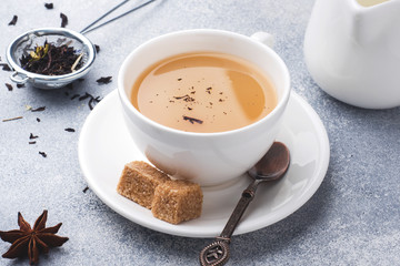 Cup of tea with milk, brown anise sugar on a grey table.