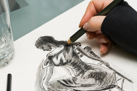 The artist at work. A fragment of a drawing of a girl made with a pencil. A woman's hand draws on a piece of paper.