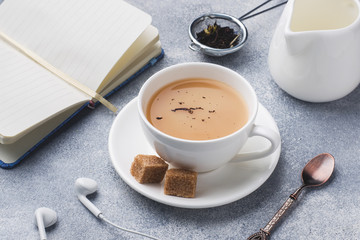 Cup of tea with milk, brown anise sugar and a notebook on a grey table.