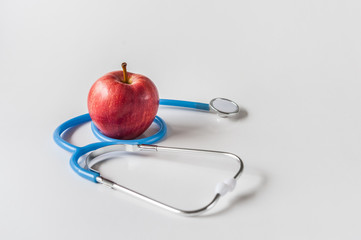 Blue stethoscope on white background with red apple. Healthcare and medical concept. World Health Day.