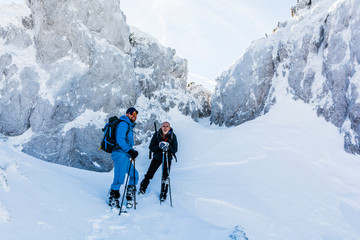 Fototapeta na wymiar Wanders with trekking sticks rest under an icy rock.