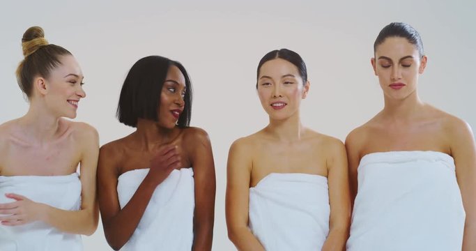 Slow motion of beautiful young smiling women of different ethnicities with perfect firm and slim body in white bathing towels whispering their beauty secrets in the ear and having fun.
