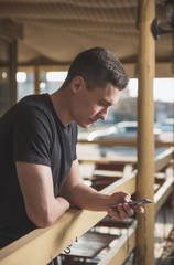 A handsome, slender young man in a black t-shirt on the street uses a smartphone and speaks on it