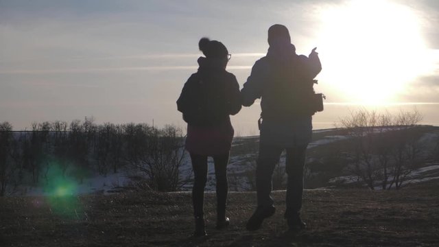 Happy couple man and woman tourist at top of mountain at sunset outdoors during a hike. Silhouettes of two hikers with backpacks enjoying sunset. The concept of travel and active lifestyle.