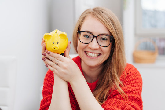 Happy young woman holding a yellow piggy bank