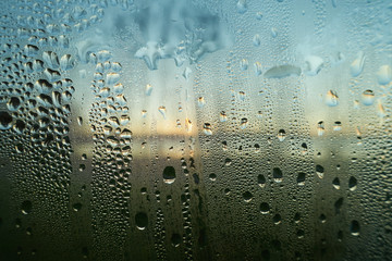 Raining water drops on a wet window closeup image. Condensed moisture on a glass surface in the...