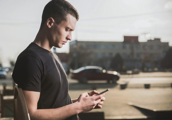 A handsome, slender young man in a black t-shirt on the street uses a smartphone and speaks on it - 256601085