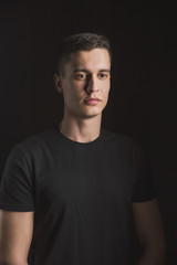Beautiful, slender young man in black t-shirt on black background and on the street
