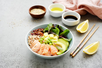 Salmon poke bowl with salad, avocado, edamame beans, pineapple and sesame Brown rice poke bowl Top view, clean eating concept Traditional Hawaiian dish