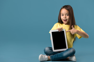 cute little child girl holding blank tablet computer on blue background