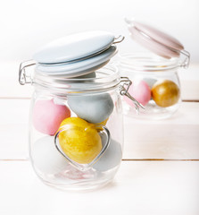 Easter background with pink, blue, golden Easter eggs in glass jar on white wooden desk