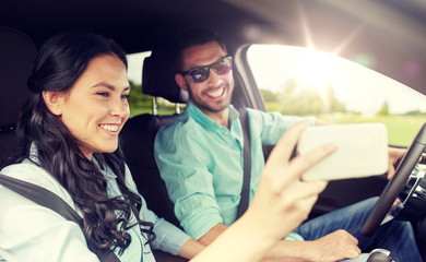 road trip, leisure, couple, technology and people concept - happy man and woman driving in car and taking selfie with smartphone