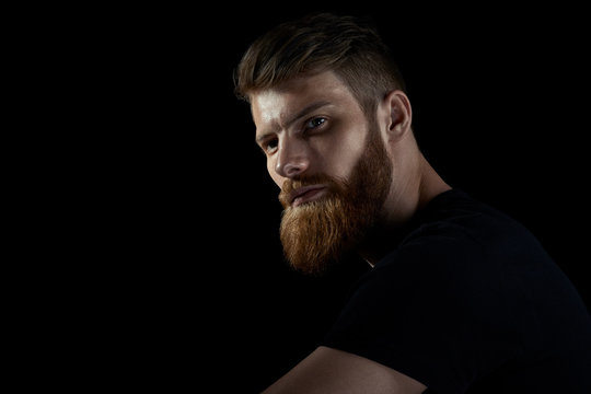 Dramatic light studio shot of young caucasian bearded stylish man Handsome hairstyling male portrait over black background Free copy space template.