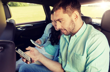 road trip, travel, technology and people concept - happy couple with smartphones riding on back seat of taxi car
