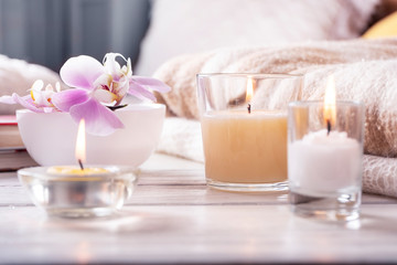 Fototapeta na wymiar Composition of three candles, orchid in vase on white wooden tray in front of bed. Home interior detailes close up.