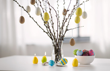 holidays and object concept - pussy willow branches decorated by easter eggs in vase and candles on...