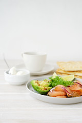 Avocado and smoked salmon on plate. Healthy breakfast. White wooden background