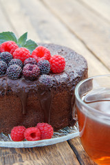 Homemade chocolate cake decorated with black and red raspberries on glass plate with cup of tea.