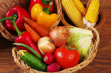 Vegetables, corn, tomatoes, onions, parsley, radishes, cucumbers, carrots, peppers in a basket on a wooden table