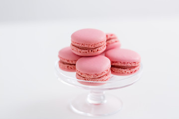 sweets, pastry and food concept - pink macarons on glass confectionery stand over white background