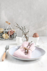 Easter table setting idea, minimal decoration - pink napkin, fork, coloured eggs in white basket, willow banch, white wooden table