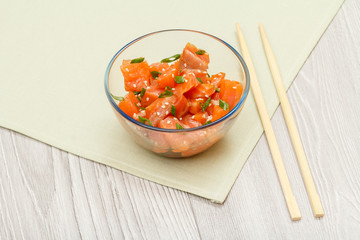 Hawaiian salmon poke with green onions and sesame seeds in glass bowl.