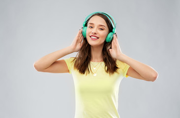music, technology and people concept - happy young woman or teenage girl with headphones over grey...