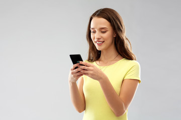 technology and people concept - smiling young woman or teenage girl in blank yellow t-shirt using smartphone over grey background