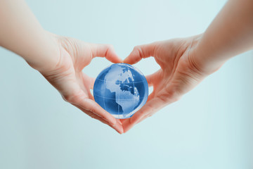 Hands in shape of heart  holding blue glass globe of South and North America