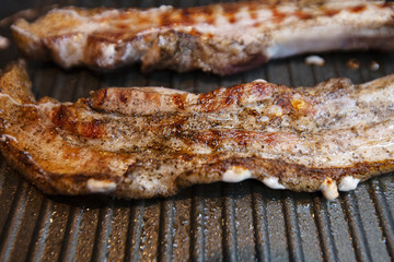 Two pieces of pork meat sprinkled with pepper, fry in a frying pan on two side.