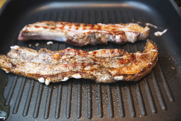 Two pieces of pork meat sprinkled with pepper, fry in a frying pan on two side.