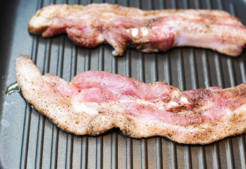 Two pieces of pork meat sprinkled with pepper, fry in a frying pan on one side.