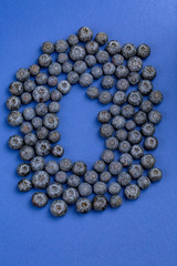 A view from above on delicious and juicy blueberries on a blue background. Tasteful, raw and ripe blueberries full of vitamins.