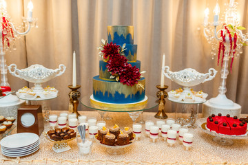 Candy bar. blue wedding cake decorated by flowers standing of festive table with deserts, strawberry tartlet and cupcakes. Wedding.