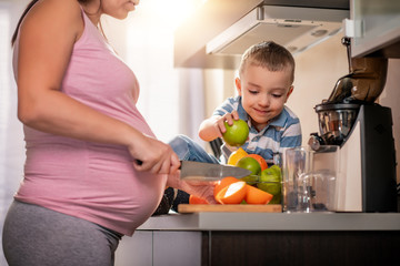 Mother and her kid making fresh orange juice in kitchen