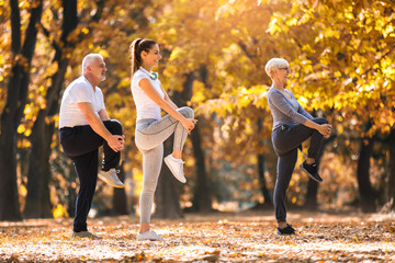 Senior man and woman and young female instructor  workout on fresh air. Outdoor activities, healthy...
