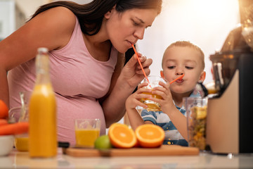 Obraz na płótnie Canvas Mother and her kid making fresh orange juice in kitchen