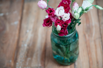 Bouquet of red Eustoma in glass jar on wooden boards