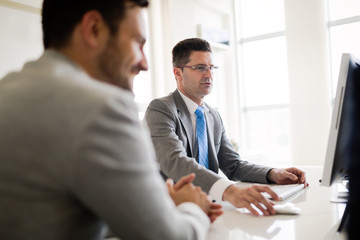 Image of two handsome businessmen using computer at meeting