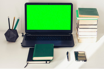 Obraz na płótnie Canvas Green screen laptop, stack of books, notebook and pencils on white table, education office concept background.