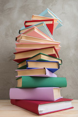 Education and reading concept - group of colorful books on the wooden table, concrete wall blackboard