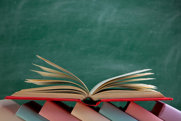 Education and reading concept - group of colorful books on the wooden table in the classroom, blackboard background