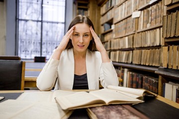 Tired girl in the reading room of the library to read books to prepare for the exam holding her head