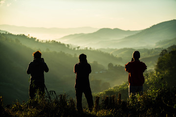 Silhouette of three photographers taking landscape pictures of morning mist on the mountain