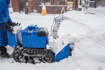 Man operating snow blower machine on the sidewalk in winter