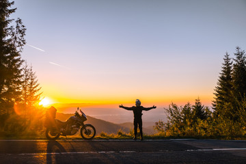 Silhouette of man biker and adventure motorcycle on the road with sunset light. Hands up. enjoy momment. Top of mountains, tourism motorbike, vacation active lifestyle. Transfagarasan, Romania.