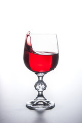 Red wine splashing in wine glass on light background. .