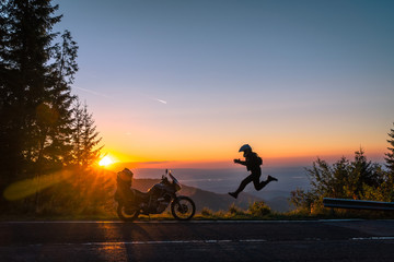 Silhouette of man biker and adventure motorcycle on the road with sunset light background. leap with joy. Top of mountains, tourism motorbike, vacation active lifestyle. Transfagarasan, Romania.