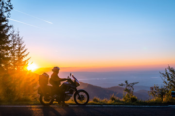 Silhouette of man biker and adventure motorcycle on the road with sunset light background. Top of mountains, tourism motorbike, vacation active lifestyle. Transfagarasan, Romania. - obrazy, fototapety, plakaty