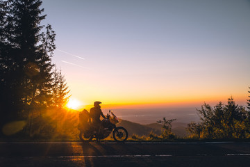 Silhouette of man biker and adventure motorcycle on the road with sunset light background. Top of...